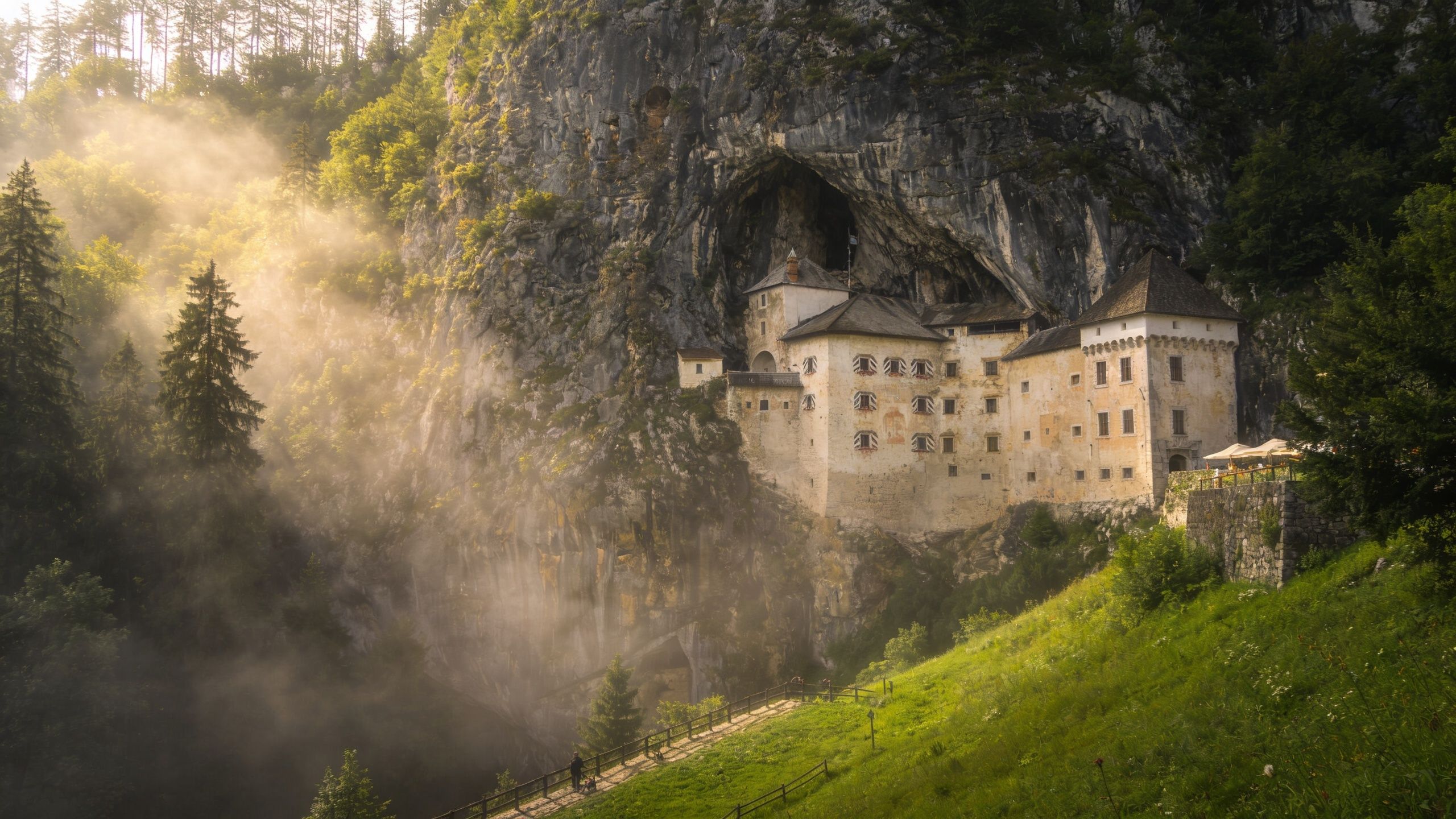 The historic Predjama Castle built into a massive cliffside cave entrance surrounded by misty forest landscapes.