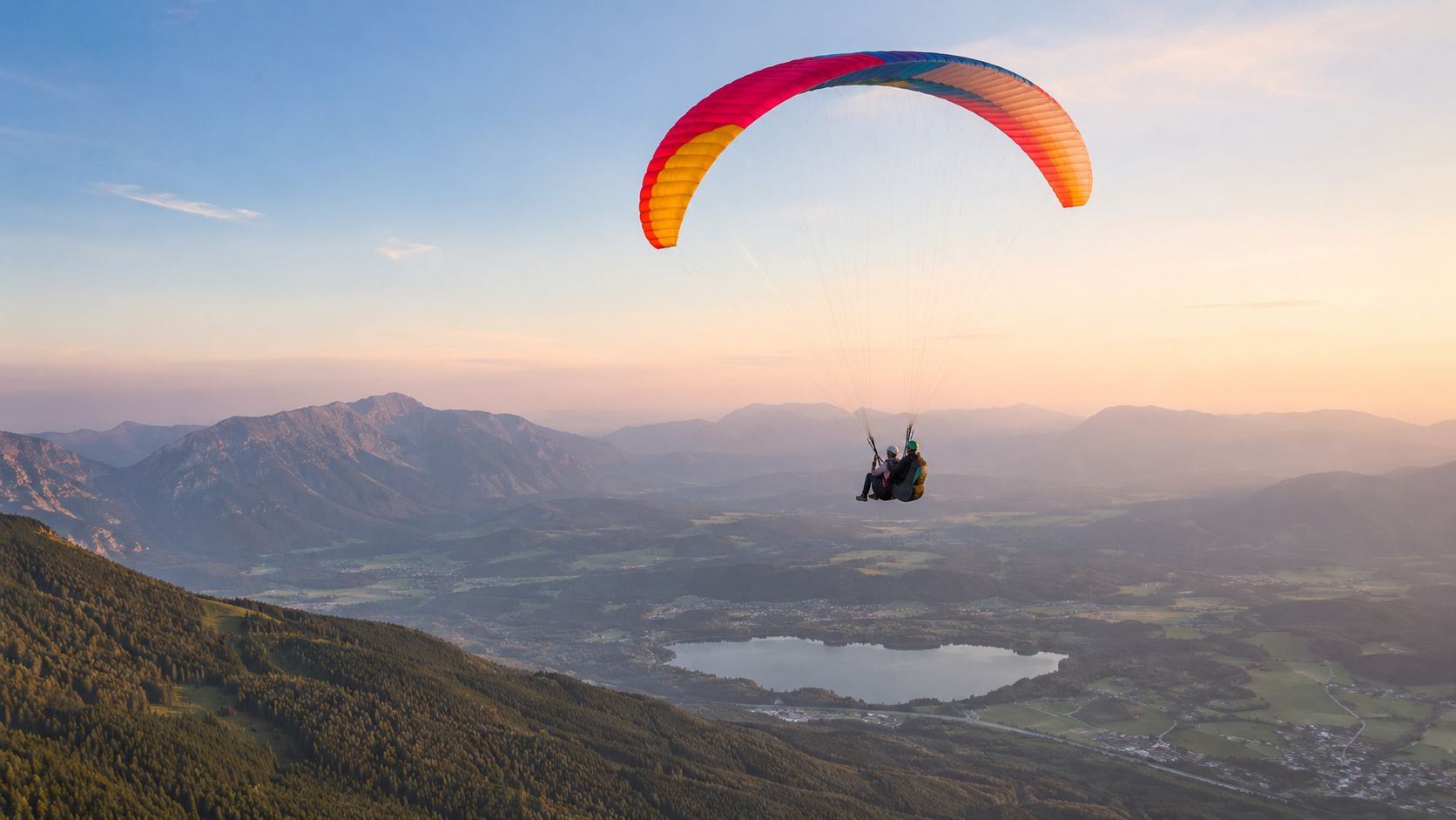 Two people paragliding above a serene mountain lake near Kranjska Gora during a beautiful sunset.