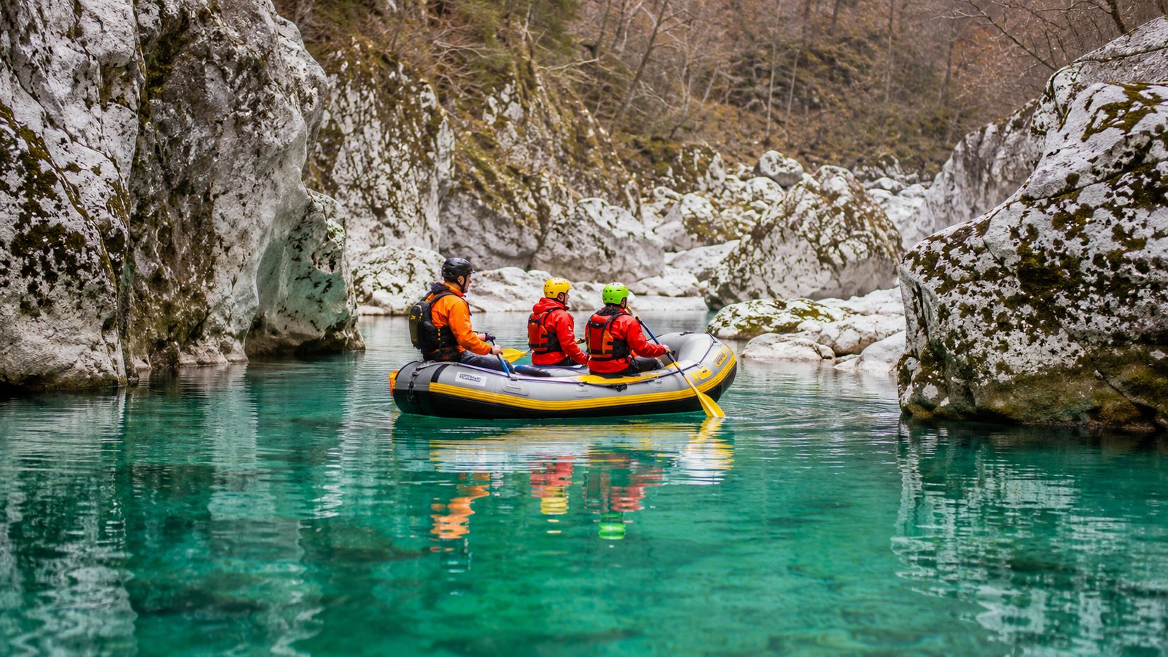 Three people in a yellow raft navigating turquoise waters through a scenic rocky canyon in winter.