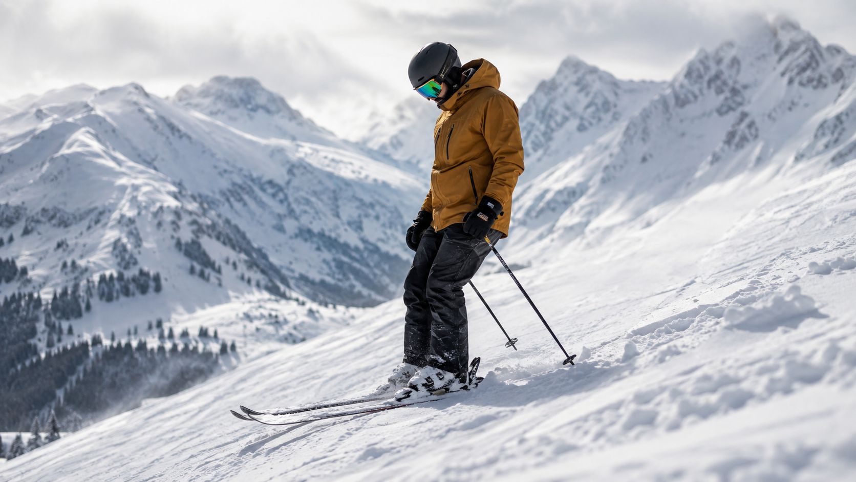 A skier in a yellow jacket and black pants skiing down a scenic snow-covered mountain slope