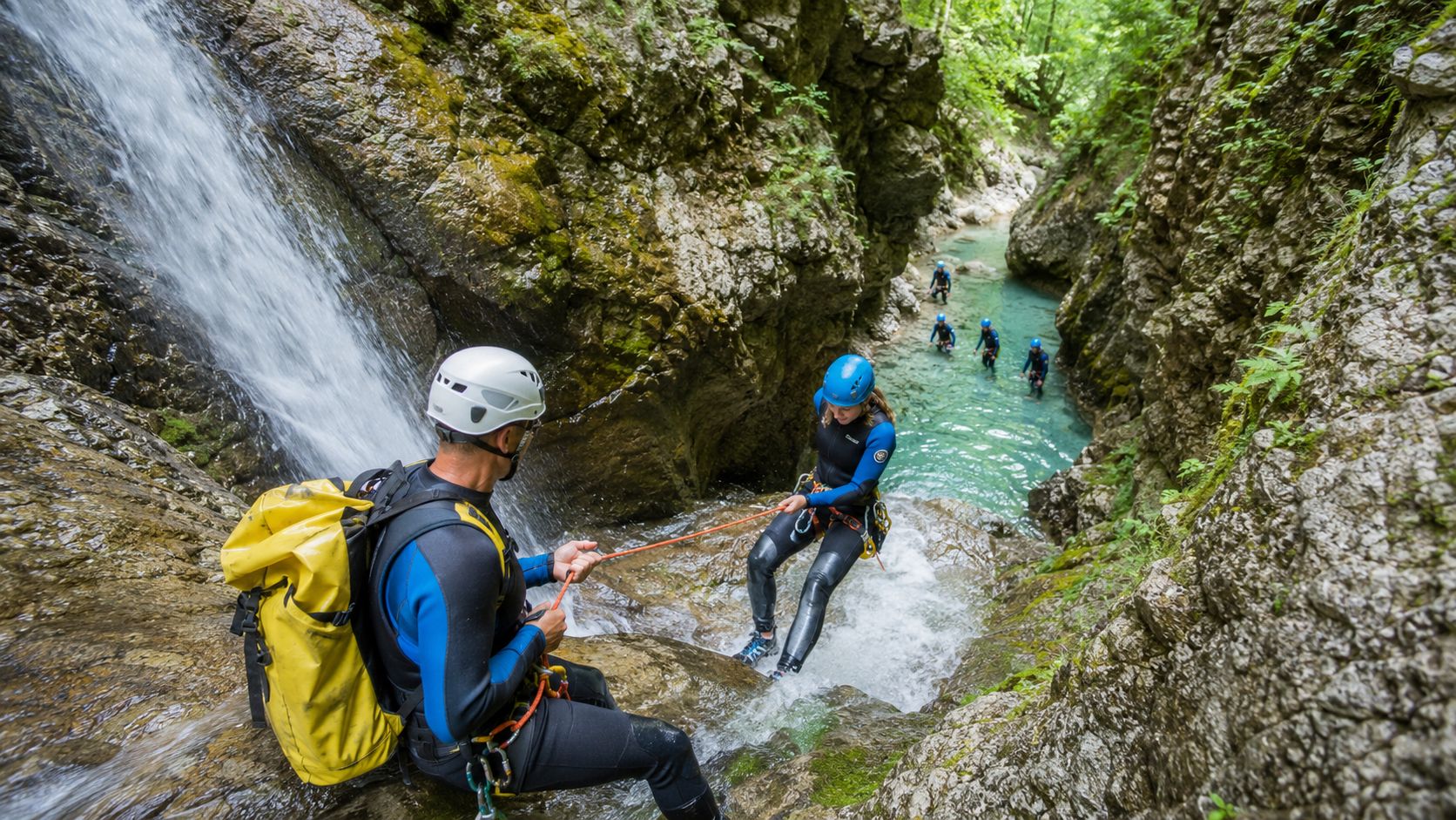 Canyoning guide assisting a woman as she rappels down a waterfall in a picturesque rocky canyon